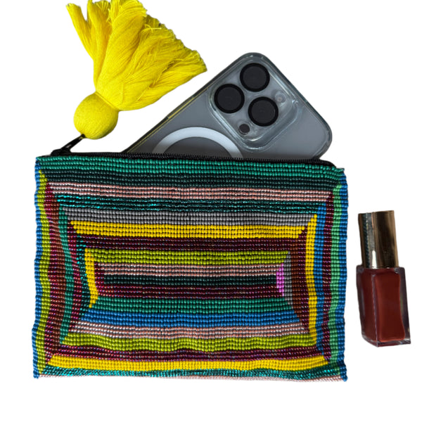 Colorful striped pouch with a yellow tassel, remote control, and nail polish on a gray surface